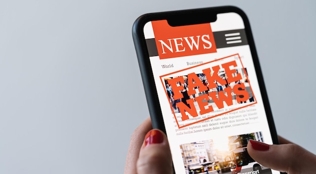 Online nepnieuws op een mobiele telefoon Close-up van een vrouw die nepnieuws HOAX of artikelen leest in een smartphone-schermtoepassing Hand met slim apparaat Mockup-website Valse krantenportaal