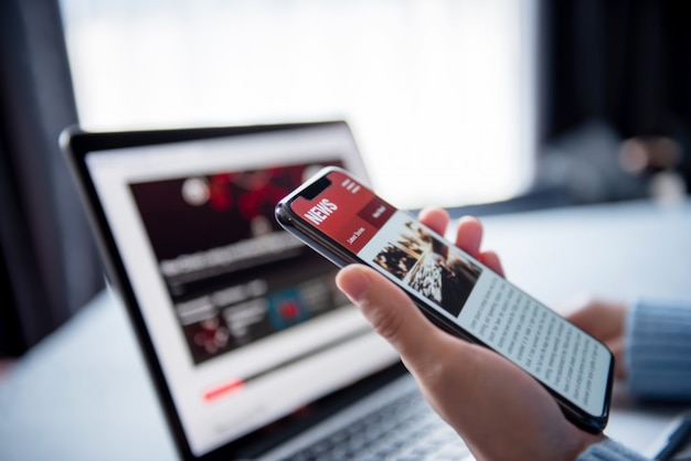 Online News On A Smartphone And Laptop. Mockup Website. Woman Reading News Or Articles In A Mobile Phone Screen Application At Home. Newspaper And Portal On Internet.