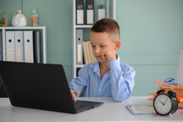 Online onderwijs op afstand Een schooljongen studeert thuis en maakt huiswerk op school