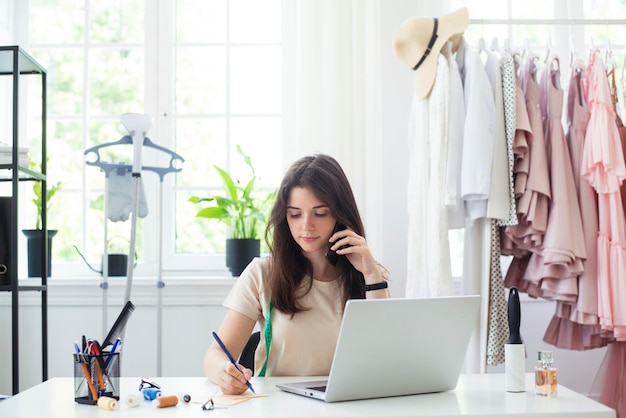 Online ordering tailoring from seamstress, fashion designer, tailor. woman fashion designer talking on the phone, advising the client in dressing workshop.