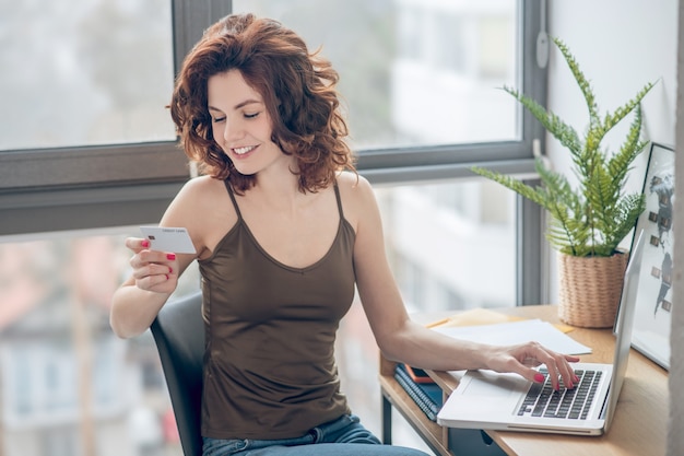 Online payments. Dark-haired pretty woman holding a credit card and planning to make online payments