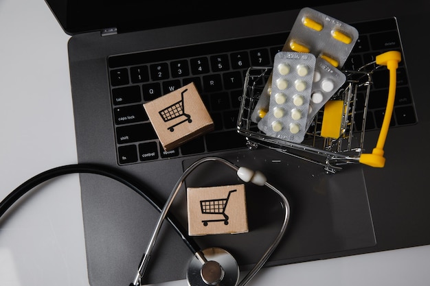 Фото Онлайн-аптека и тележка для доставки лекарств с коробками для таблеток и стетоскопом на ноутбуке