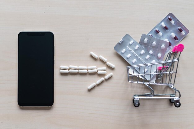 온라인 약국 개념 전화로 온라인 약 구매 의약품 배달 캡슐이 있는 미니 트롤리 및 검은색 빈 화면이 있는 스마트폰
