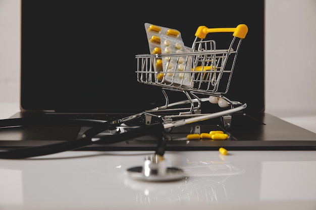 Online pharmacy Trolley with pills and stethoscope on a laptop