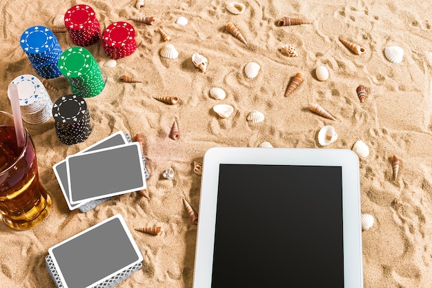 Foto gioco di poker online sulla spiaggia con tavoletta digitale e pile di fiches vista dall'alto