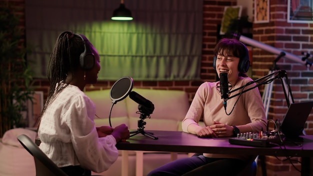 Online radio host doing high five hand gesture with african\
american influencer during live podcast in living room home studio.\
two women with headphones high fiving while recording internet talk\
show