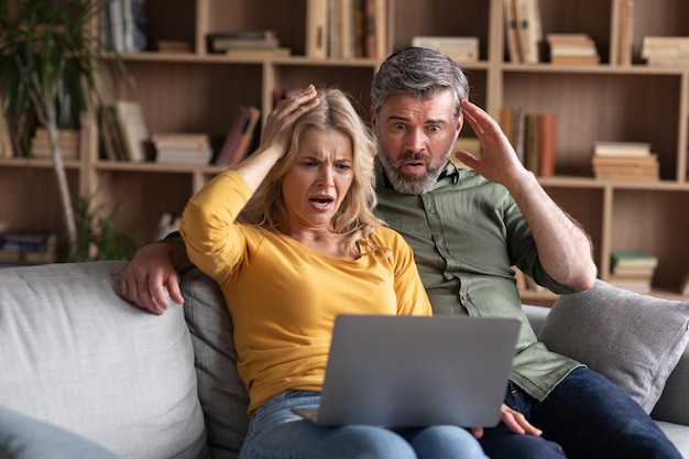 Online Scam Emotional middle aged couple looking at laptop screen with shock