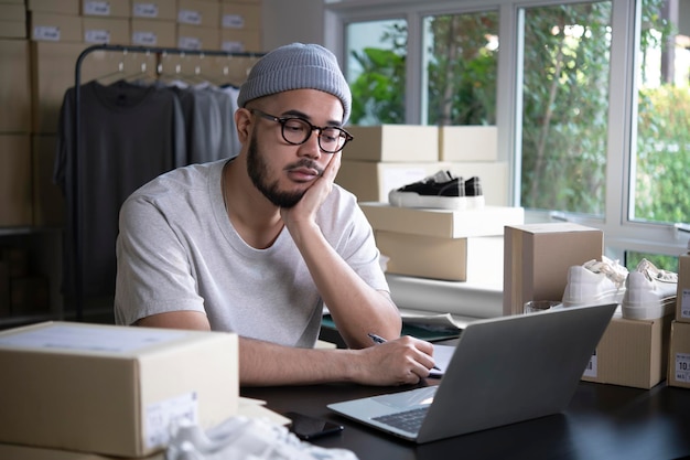 Online seller entrepreneur in a warehouse looking at laptop and worrying about ecommerce business due to lack of sales and customers