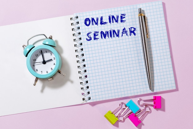 An online seminar is an inscription, a phrase written in a Notepad that lies on a light background along with a pen and an alarm clock.