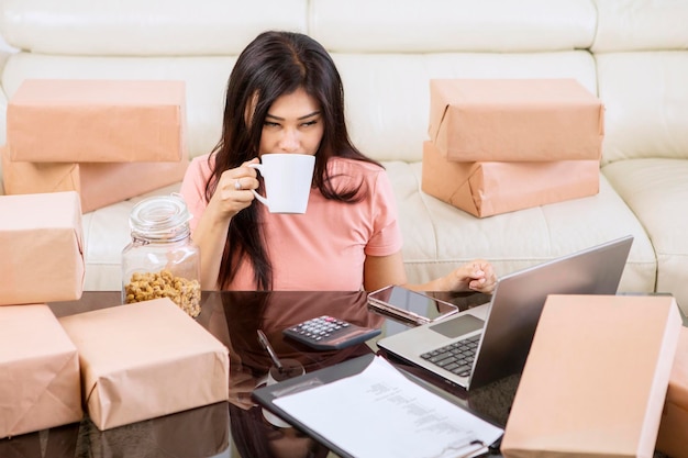 Online shop owner works and drinks coffee at home