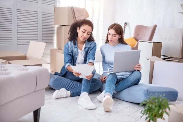 Online shopping. Charming young girls sitting on the floor and looking through color charts, selecting paint for the walls online