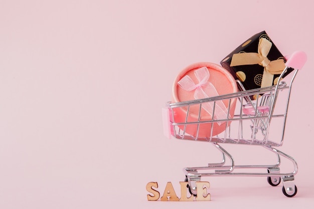 Online shopping concept, shopping cart with gift boxes in pink table with copy space