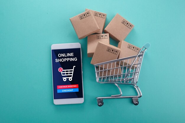 Online shopping concept. Smart phone with shopping cart on mint background. Top view.