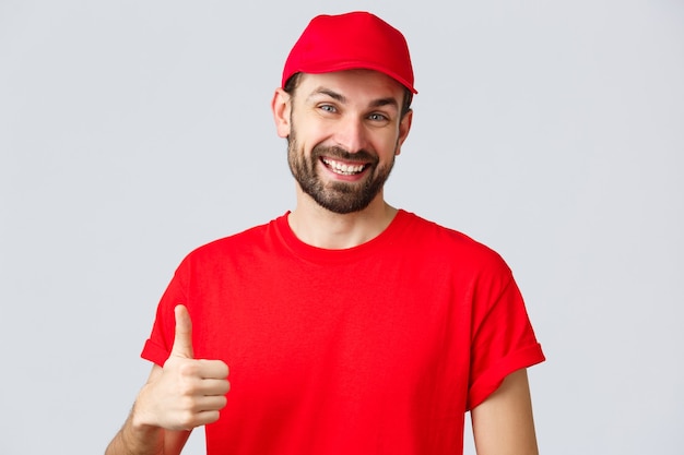 Online shopping, delivery during quarantine and takeaway concept. Friendly, cheerful courier in red cap and t-shirt uniform, encourage make internet orders, thumb-up in approval or recommendation.