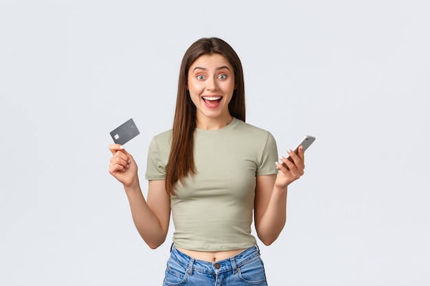 オンラインショッピング、家庭のライフスタイルと人々の概念。興奮した幸せな女性は、クレジットカードとスマートフォンを驚かせて、特別割引のある優れたインターネットストアを見つけました。