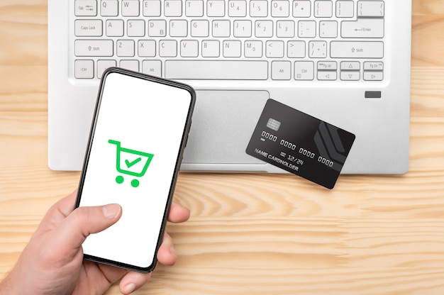 Online shopping, phone laptop and credit card. Top view man at wooden desk with  phone