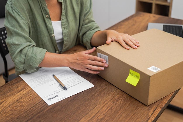 Foto rimborso degli acquisti online una donna mette un adesivo a codice a barre su un pacco di cartone per la restituzione