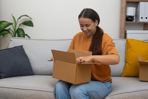 Online shopping smiling lady explores delivery satisfaction with sofa and opened cardboard parcel