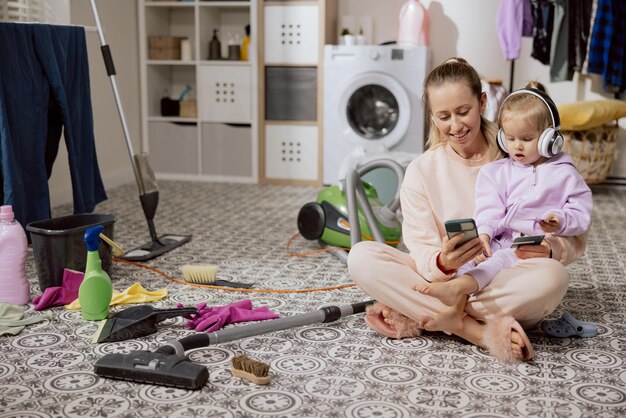 家の掃除をしながらオンライン ショッピングをする女性と若い娘が休憩中に音楽を聴く