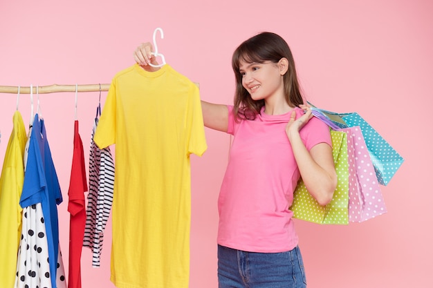 Online shopping. young asian woman with shopping bags tries on colorful fashion clothes in the store. pink background