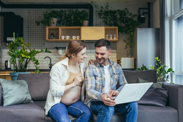 Online shopping Young family pregnant woman and man make an online purchase order from a laptop holding a credit card Sitting at home on the couch Very happy satisfied