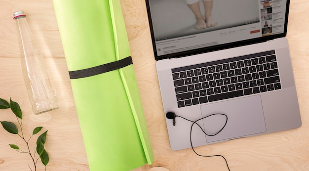 Online sport or training course concept top view Laptop with yoga mat and glass bottle of water on the wood floor