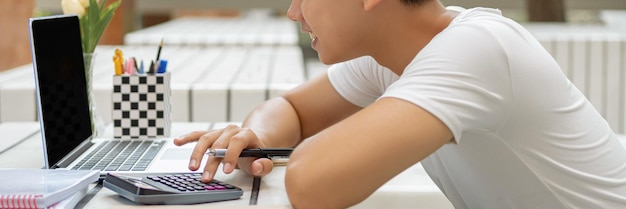 Online studeren concept de man in effen wit T-shirt voelt zich best gelukkig en houdt de rekenmachine vast voor het berekenen van getallen in de boekhoudklas.