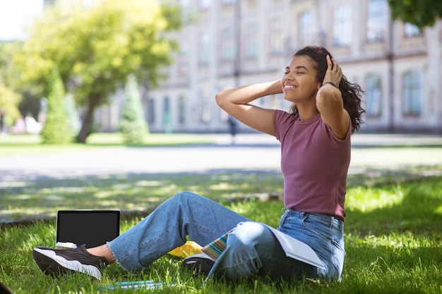 Online studeren. Een meisje in vrijetijdskleding zittend op het gras in het park en studeren