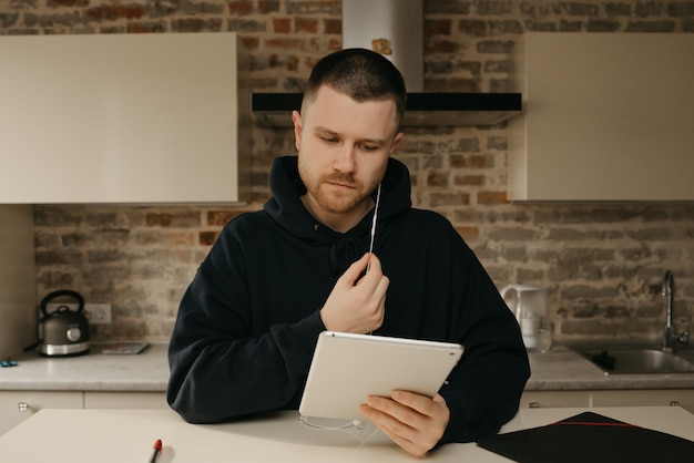 Online studeren op afstand. Een man met een baard die op afstand op zijn tablet studeert. Een man die naar een webinar kijkt.