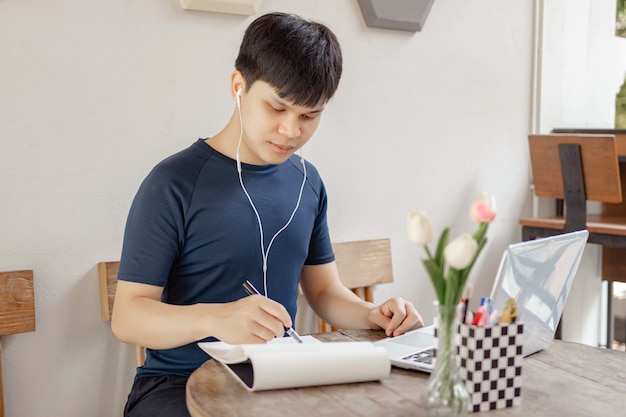 Online studieconcept een zwartharige student die zijn huiswerk doet door informatie op internet te zoeken en deze zwarte pen te gebruiken om de conclusie van zijn onderzoek op papier te schrijven.