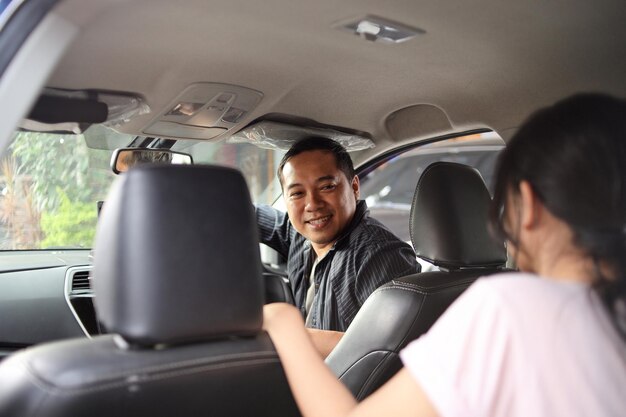 Online taxi driver smiling while turning over to the backseat looking and talking with customer