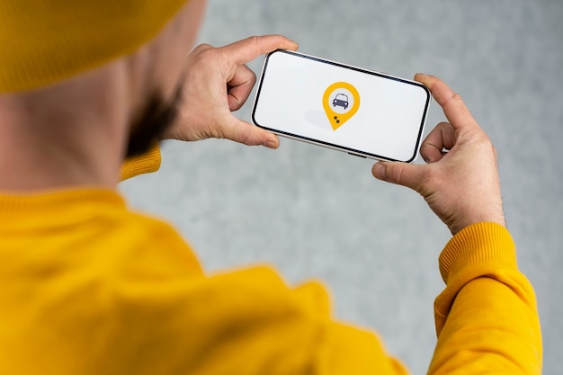 Online taxi on your phone. a man holds a smartphone with a\
white screen and a geolocation and location icon for a taxi.