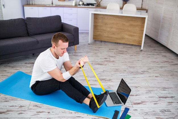 Online training. Man doet oefening met elastiekjes thuis, vrije ruimte. Thuis sporten