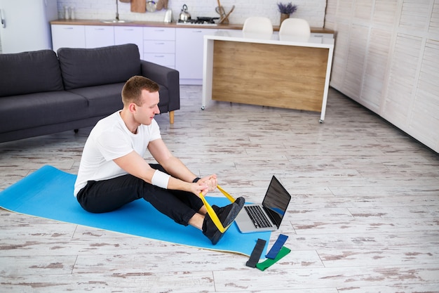 Online training. Man doing exercise with rubber bands at home, free space. Doing sports at home