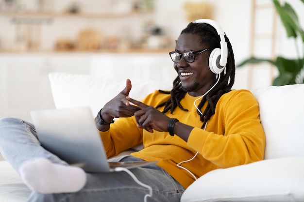 Online tutoring cheerful black man in headphones making video\
conference on laptop