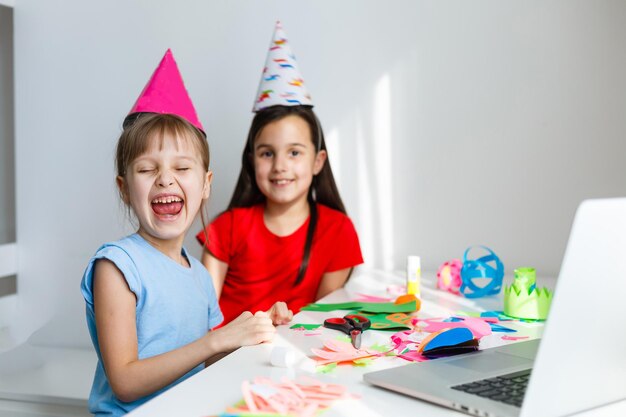 Online verjaardagsfeestje voor kinderen. kleine meisjes in jurken, hoed vieren vakantie met vrienden. conferentie, videogesprek op laptop, computer. quarantaine, coronavirus pandemie covid-19.