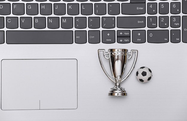 Online wedden op sport. Voetbalbal en kampioenskop op laptop toetsenbord. Bovenaanzicht. plat leggen