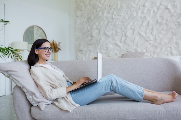 Online werk jonge zakenvrouw in glazen freelancer die thuis werkt op een laptop die comfortabel ligt