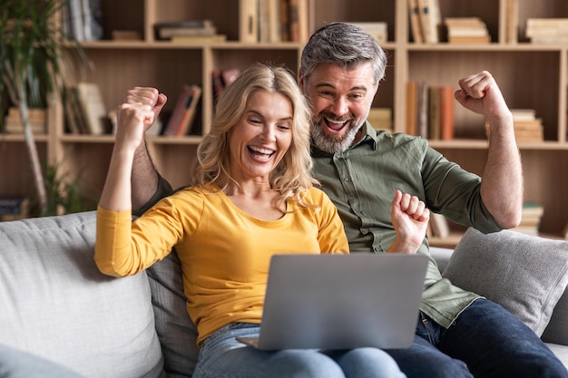 Online win portret van dolblij koppel van middelbare leeftijd dat succes viert met laptop