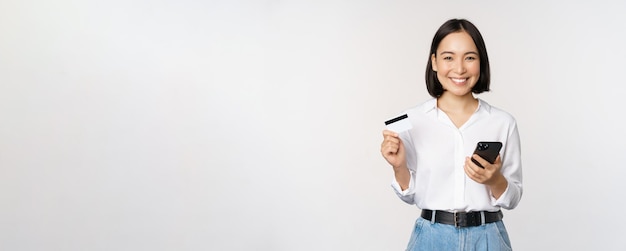 Online winkelconcept Afbeelding van een jonge Aziatische moderne vrouw met creditcard en smartphone die koopt met een smartphone-app die contactloos betaalt over een witte achtergrond