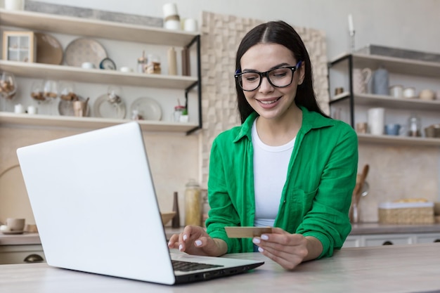Online winkelen een jonge mooie vrouw met een bril en een groen shirt zit thuis met een laptop
