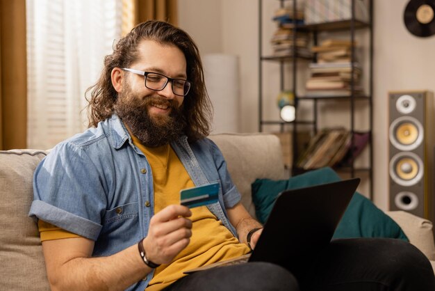 Online winkelen een lachende bebaarde man betaalt met een bankpas bij een online winkel