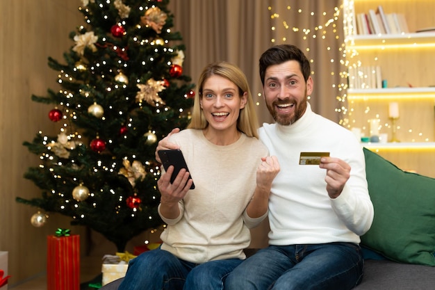 Online winkelen gelukkig jong stel thuis bij de kerstboom een man en een vrouw hebben een tegoed