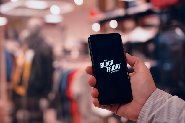 Online winkelen op Black Friday. Een man houdt een smartphone in zijn handen tegen de achtergrond van een modieuze kledingboetiek.