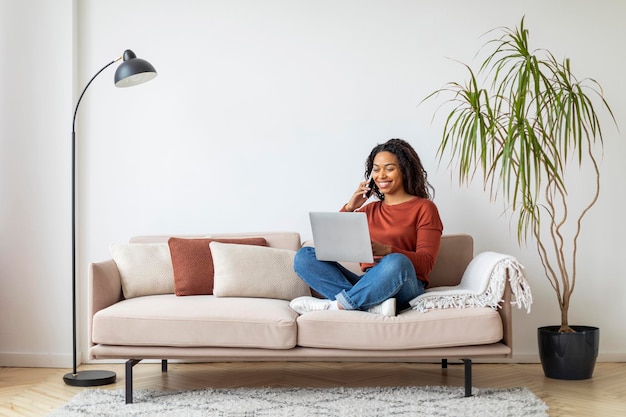 Online work young black woman working with laptop and cellphone at home