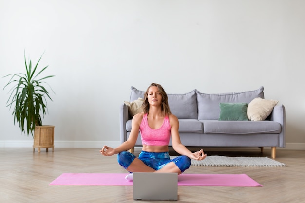 Online yoga lesson. Woman in lotus position in front of laptop monitor.