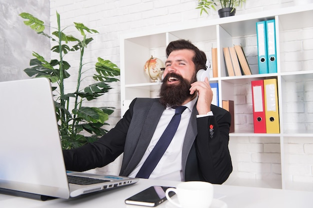 Online zaken doen. Detailhandelaar gebruikt laptop en koptelefoon. Handelsbedrijf. Bebaarde man werk in kantoor. Zakelijke communicatie. Nieuwe technologie. E-commerce. Videovergaderen.