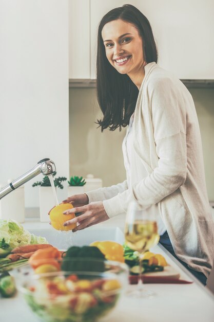 私のサラダには清潔で新鮮な野菜だけを。サラダのために野菜を洗って、台所に立っている間笑顔の美しい若い女性