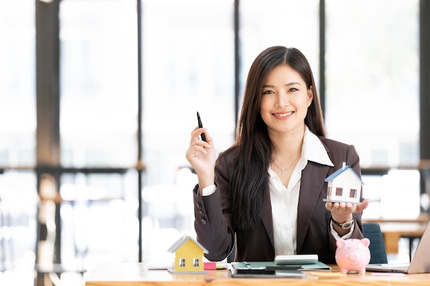 Onroerend goed agent met model van het huis zit op het kantoor glimlachen naar de camera