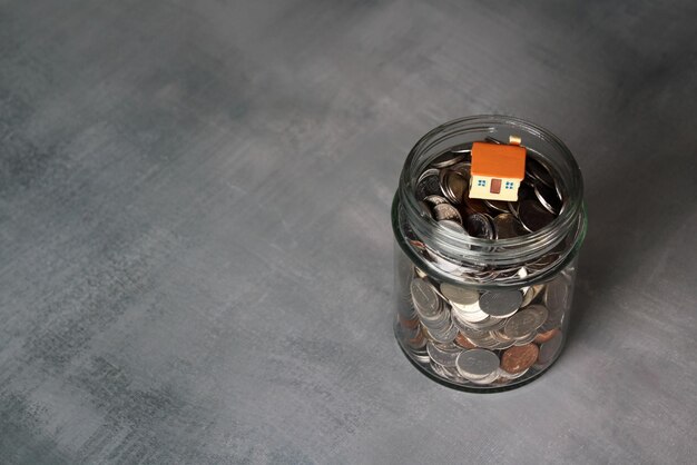 Onroerend goed en financieel concept Close-up beeld van munten in glazen pot met miniatuurhuis